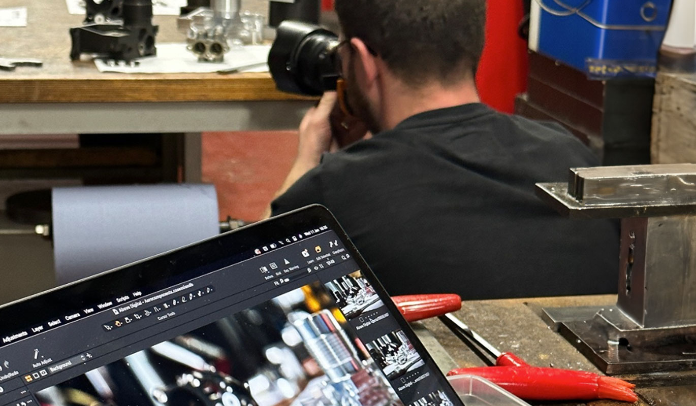 A photographer capturing close-up shots of mechanical parts on a workbench, with a laptop in the foreground showing the photo review.