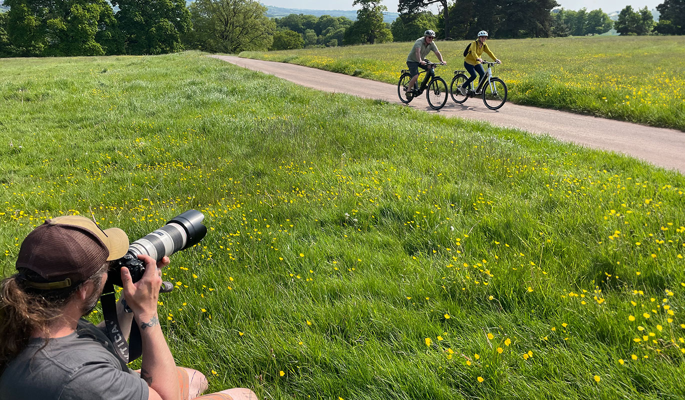 A photographer with a telephoto lens capturing two people on electric bicycles riding along a country path.