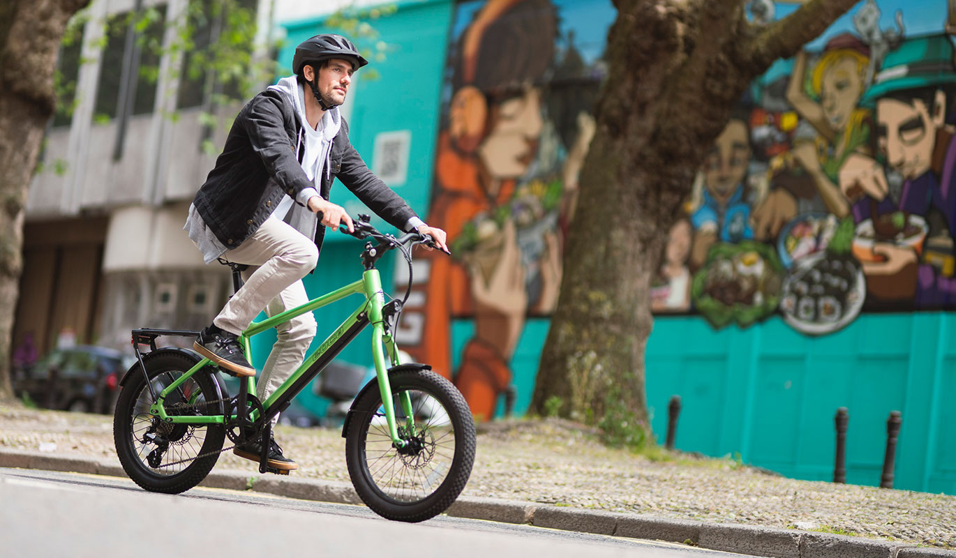 A man wearing a helmet riding a bright green electric bike on a city street in front of a colourful mural.