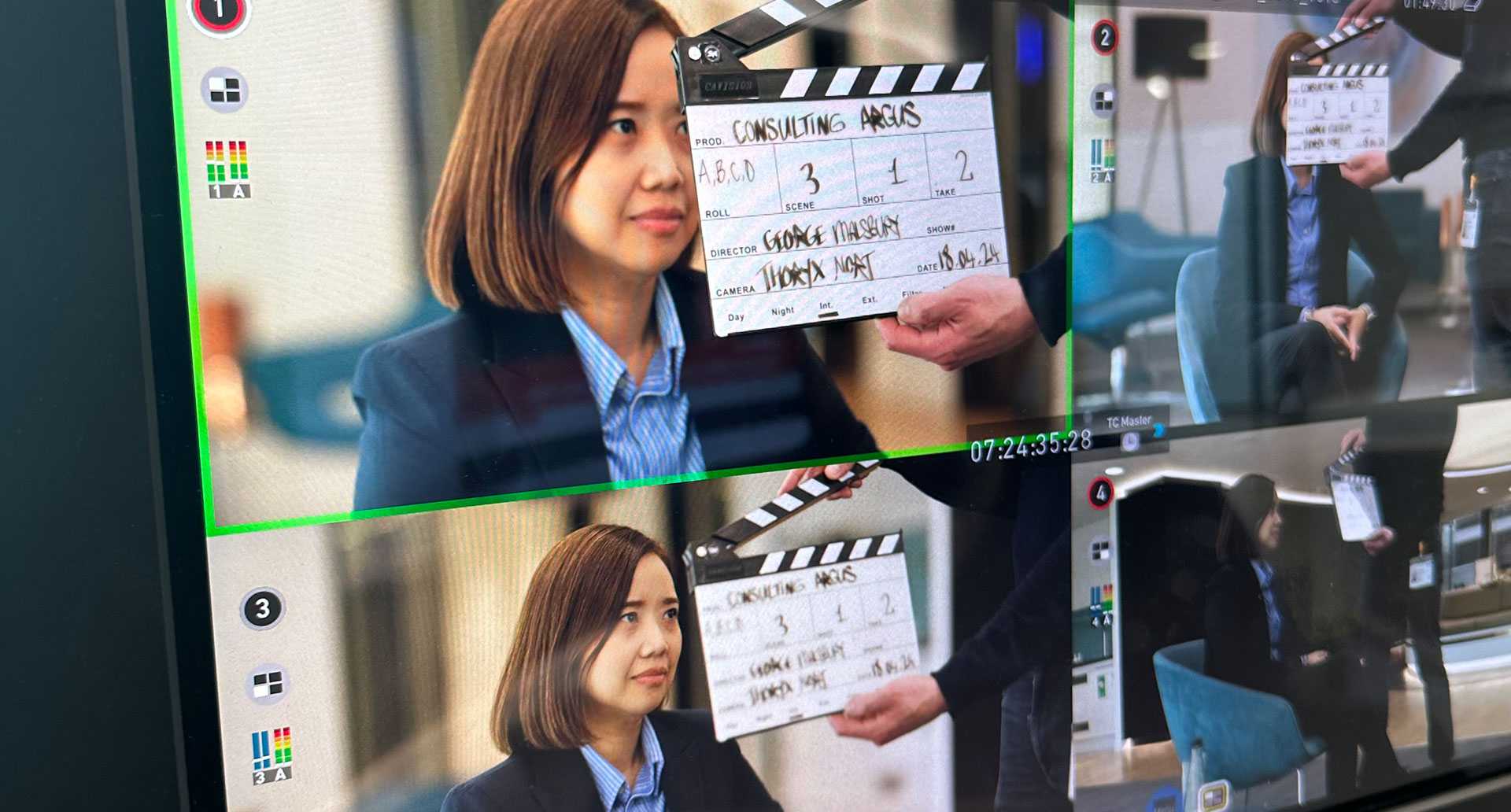 A close-up of a production monitor displaying four camera angles of an interviewee, with a hand holding a film clapperboard in front of the lens.