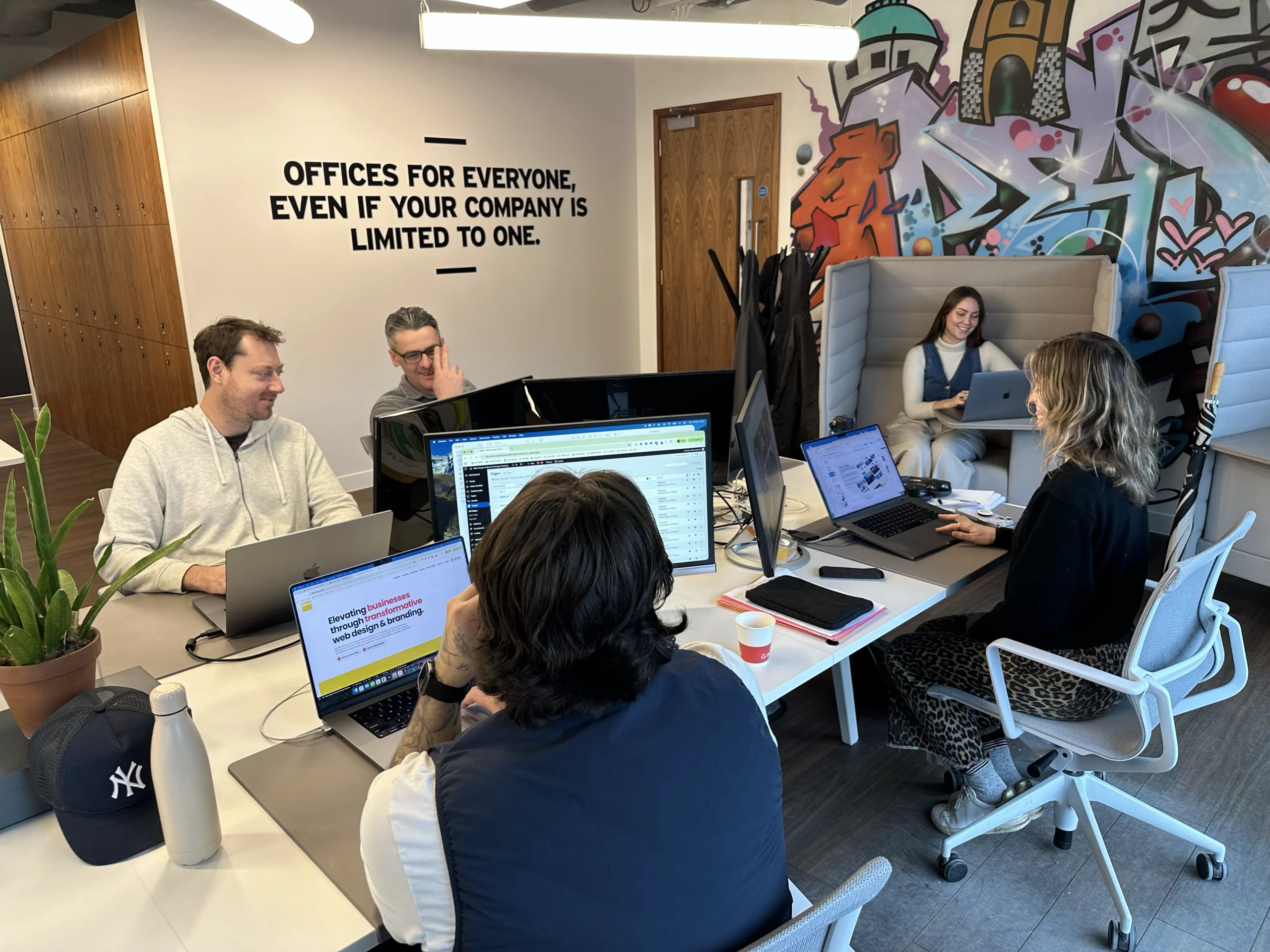 The Above Digital Team sit in-office, collaborating at desks, and smiling